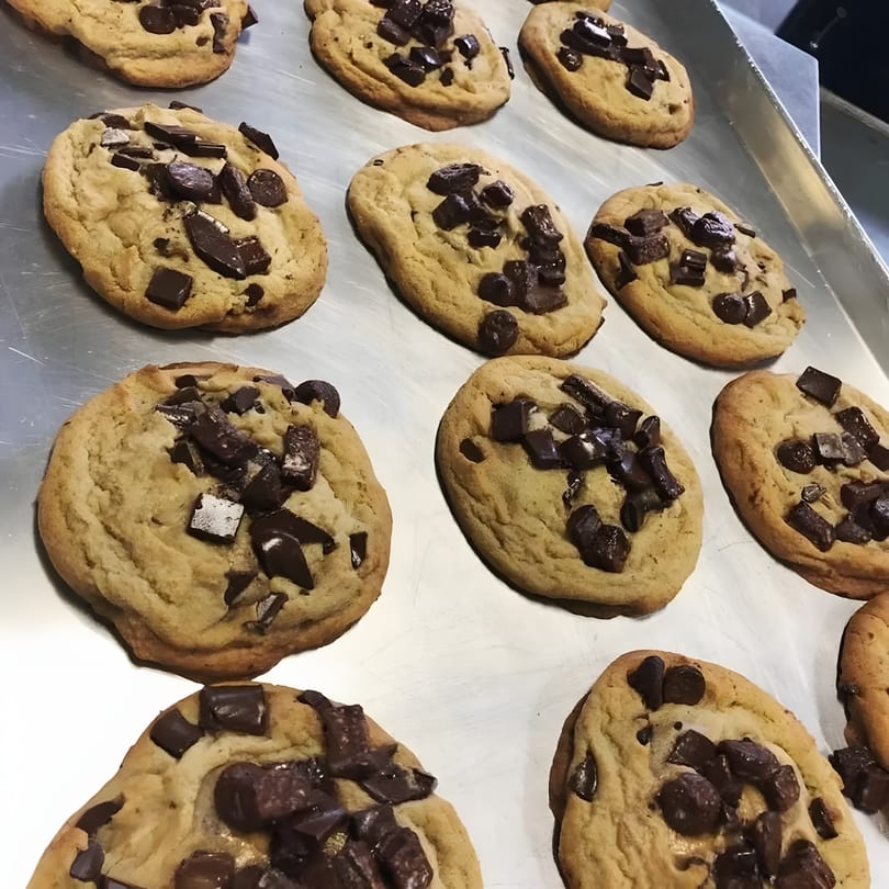 Freshly baked chocolate chip cookies with large chocolate chunks on a metal baking sheet.