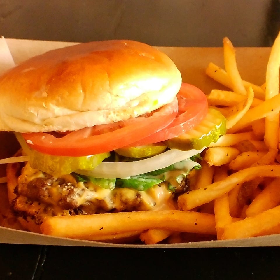 A juicy Ella's Kitchen + Wine Bar burger with fries, topped with lettuce, tomato, onion, and pickles.